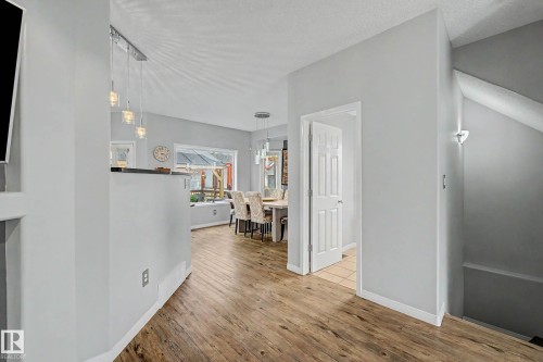 Open-concept living space with wood-finish flooring, a contemporary linear pendant light, and a dining area visible through a wide opening - 9130 100A Avenue Nw, Edmonton, AB - Indoor Photo Showing Other Room