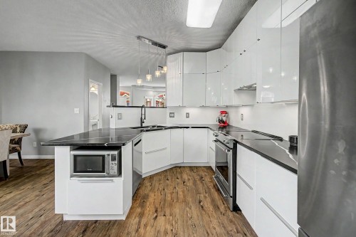 Contemporary kitchen featuring white flat-panel cabinetry, black countertops, stainless steel appliances, a modern pendant light fixture, and wood-finish flooring - 9130 100A Avenue Nw, Edmonton, AB - Indoor Photo Showing Kitchen With Upgraded Kitchen