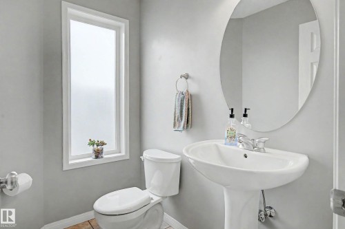 Powder room featuring a pedestal sink, round wall mirror, and a privacy window - 9130 100A Avenue Nw, Edmonton, AB - Indoor Photo Showing Bathroom