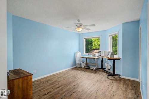 Spacious room featuring wood-finish flooring, light blue walls, and a white ceiling fan with integrated lighting - 9130 100A Avenue Nw, Edmonton, AB - Indoor