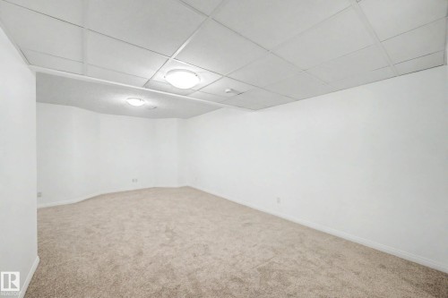Spacious room featuring neutral carpeting, white painted walls, and a dropped ceiling with integrated lighting - 9130 100A Avenue Nw, Edmonton, AB - Indoor Photo Showing Other Room