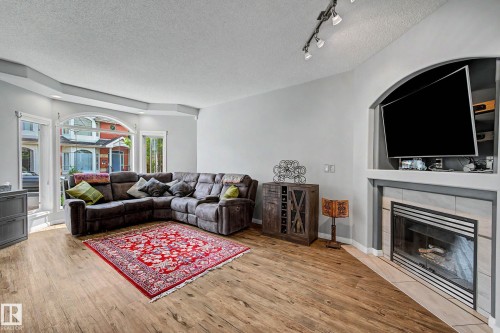 Living area featuring wood-finish flooring and a built-in fireplace with a tiled surround - 9130 100A Avenue Nw, Edmonton, AB - Indoor Photo Showing Living Room With Fireplace