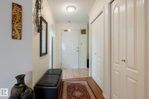 Entryway featuring white paneled doors, crown molding, and a combination of wood-finish and tile flooring - #310 17151 94A Av Nw, Edmonton, AB - Indoor Photo Showing Other Room