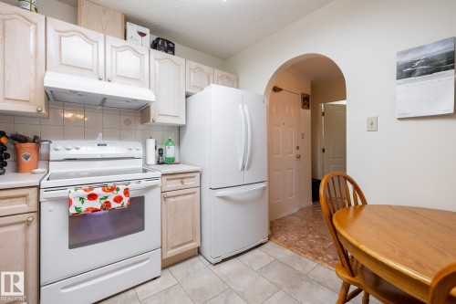 Kitchen featuring light wood-finish cabinetry, tile backsplash, white appliances, and a built-in range hood - #310 17151 94A Av Nw, Edmonton, AB - Indoor Photo Showing Kitchen