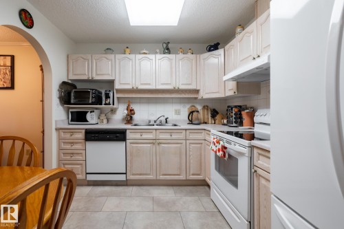 Kitchen featuring light-finish cabinetry, neutral countertops, tile backsplash, and tile flooring - #310 17151 94A Av Nw, Edmonton, AB - Indoor Photo Showing Kitchen With Double Sink