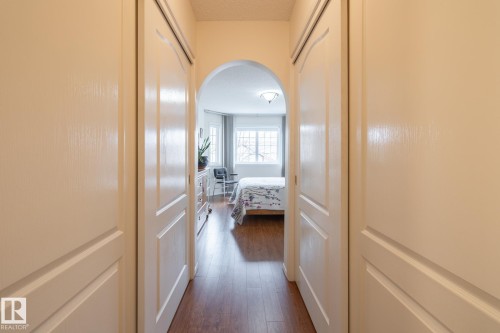 Hallway featuring wood-finish flooring, white paneled doors, and an arched entry leading to a room with natural light from multiple windows - #310 17151 94A Av Nw, Edmonton, AB - Indoor Photo Showing Other Room