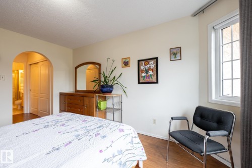 Bedroom featuring wood-finish flooring, a white-framed window with grid pattern, and an arched doorway leading to an interior space - #310 17151 94A Av Nw, Edmonton, AB - Indoor Photo Showing Bedroom