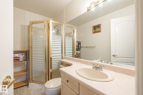 Bathroom featuring a corner shower with a gold-toned frame, a vanity with an integrated sink and light-toned countertop, a wall-mounted mirror, and a classic paneled door - #310 17151 94A Av Nw, Edmonton, AB - Indoor Photo Showing Bathroom