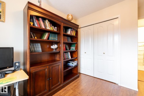 Rich wood-finish flooring complements the built-in shelving unit, offering extensive storage and display space - #310 17151 94A Av Nw, Edmonton, AB - Indoor