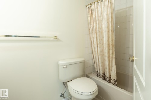 White toilet with visible plumbing, an adjacent bathtub, and tiled shower surround - #310 17151 94A Av Nw, Edmonton, AB - Indoor Photo Showing Bathroom