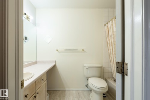 Bathroom featuring a single vanity with an integrated sink, a large wall-mounted mirror, and a toilet - #310 17151 94A Av Nw, Edmonton, AB - Indoor Photo Showing Bathroom