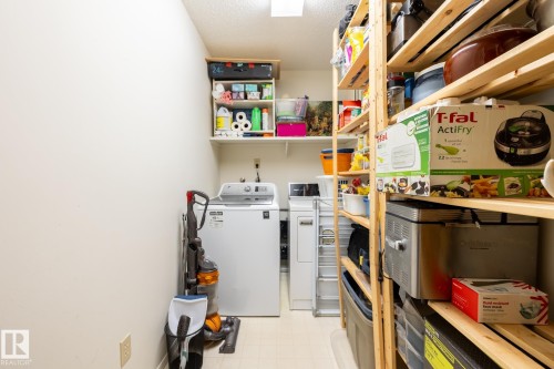 Dedicated utility room featuring a top-load washer, front-load dryer, and extensive wood shelving for organized storage - #310 17151 94A Av Nw, Edmonton, AB - Indoor Photo Showing Laundry Room