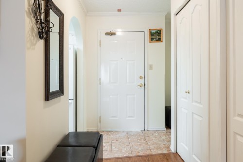Entryway featuring a paneled door, tile flooring, crown molding, and bi-fold closet doors - #310 17151 94A Av Nw, Edmonton, AB - Indoor Photo Showing Other Room