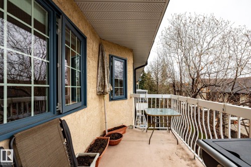 Exterior balcony featuring a textured stucco finish, dark-framed windows with grilles, and a white railing with decorative balusters - #310 17151 94A Av Nw, Edmonton, AB - Outdoor With Exterior