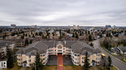 Expansive residential building featuring a U-shaped design, light-colored exterior siding, and dark roofing - #310 17151 94A Av Nw, Edmonton, AB - Outdoor With View