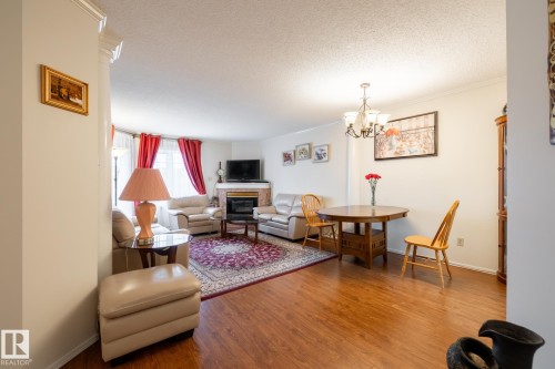 Open-concept living area featuring wood-finish flooring, a fireplace with a stone surround, and crown molding - #310 17151 94A Av Nw, Edmonton, AB - Indoor Photo Showing Living Room