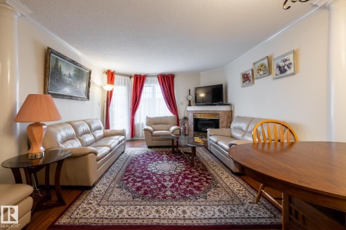 Living area featuring a fireplace with a stone surround, bay window, crown molding, wood-finish flooring, and a decorative column - #310 17151 94A Av Nw, Edmonton, AB - Indoor Photo Showing Living Room With Fireplace