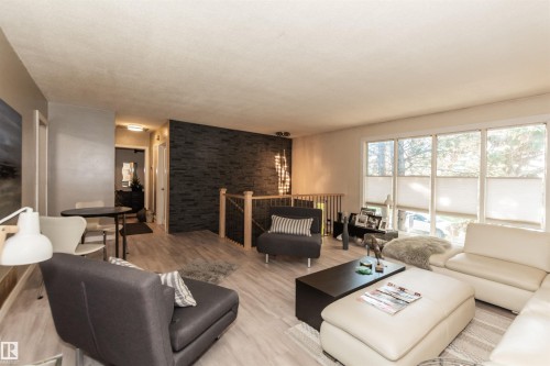 Spacious living area featuring light wood-finish flooring, a contemporary dark stone-finish accent wall, and a wood railing with metal spindles - 13208 128 Avenue Nw, Edmonton, AB - Indoor Photo Showing Living Room