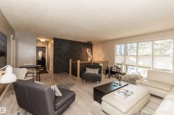 Spacious living area featuring light wood-finish flooring, a contemporary dark stone-finish accent wall, and a wood railing with metal spindles - 