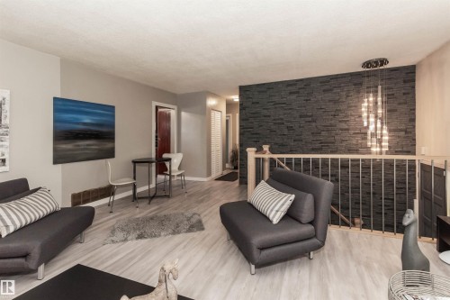 Living area featuring light wood-finish flooring, a contemporary stone accent wall, a multi-bulb chandelier, and a wood railing with metal spindles - 13208 128 Avenue Nw, Edmonton, AB - Indoor Photo Showing Other Room