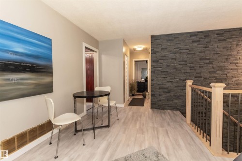 Light wood-finish flooring complements the modern stacked stone accent wall - 13208 128 Avenue Nw, Edmonton, AB - Indoor Photo Showing Other Room