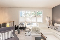 Living area featuring large multi-panel windows with cellular shades, light-toned walls with one accent wall, light wood-finish flooring, and a contemporary railing with wood top and black balusters - 