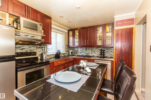 Kitchen featuring cherry wood cabinetry, a tiled backsplash, recessed lighting, and a dark stone countertop with an integrated breakfast bar - 13208 128 Avenue Nw, Edmonton, AB - Indoor Photo Showing Kitchen