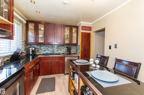 Kitchen featuring wood-finish cabinetry, black stone countertops, a mosaic tile backsplash, stainless steel appliances, and wood-finish flooring - 13208 128 Avenue Nw, Edmonton, AB - Indoor