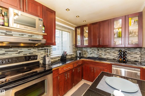 Kitchen featuring rich wood cabinetry, stainless steel appliances, dark countertops, and a mosaic tile backsplash - 13208 128 Avenue Nw, Edmonton, AB - Indoor Photo Showing Kitchen With Stainless Steel Kitchen