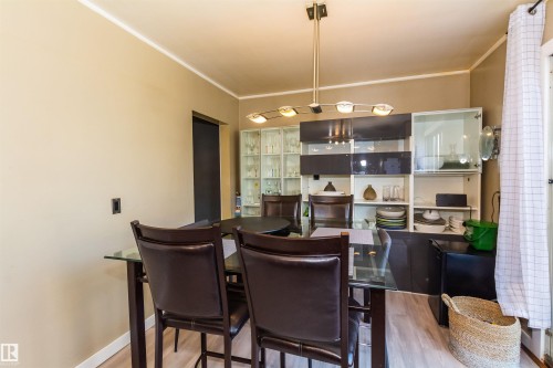 Dining area featuring light wood-finish flooring, a modern linear chandelier, and neutral wall tones - 13208 128 Avenue Nw, Edmonton, AB - Indoor