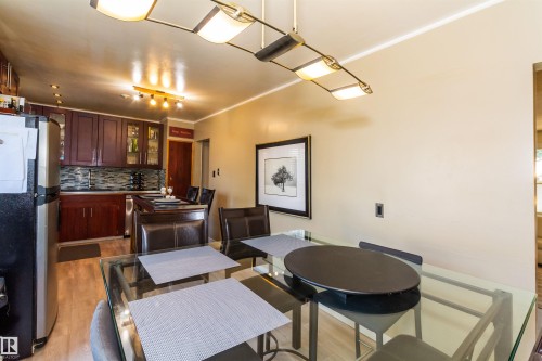 Open-concept dining area featuring a glass-top table with dark chairs, illuminated by an overhead linear light fixture - 13208 128 Avenue Nw, Edmonton, AB - Indoor Photo Showing Dining Room