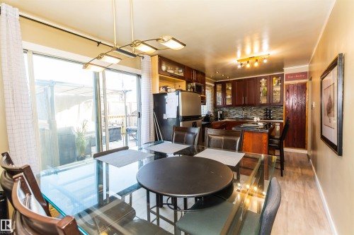 Dining area featuring a glass-top table, wood-finish flooring, and direct access to an outdoor patio through sliding glass doors - 13208 128 Avenue Nw, Edmonton, AB - Indoor Photo Showing Dining Room