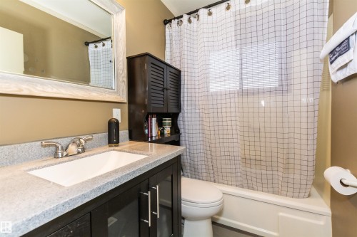 Bathroom featuring a rectangular sink set in a light-toned countertop, a dark wood-finish vanity with cabinet storage, a framed mirror, a built-in dark wood-finish storage cabinet, and a white toilet and bathtub combination - 13208 128 Avenue Nw, Edmonton, AB - Indoor Photo Showing Bathroom