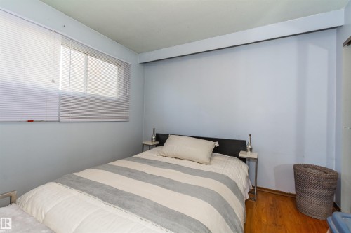 Bedroom featuring wood-finish flooring, light blue walls, a window with horizontal blinds, and a built-in closet with sliding doors - 13208 128 Avenue Nw, Edmonton, AB - Indoor Photo Showing Bedroom