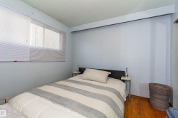 Bedroom featuring wood-finish flooring, light blue walls, a window with horizontal blinds, and a built-in closet with sliding doors - 