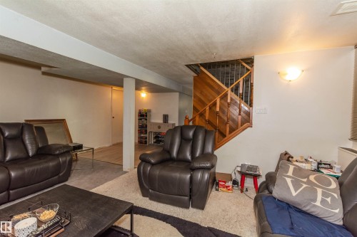 Finished lower level featuring a full wood staircase with metal balusters, overhead lighting, sconce lighting, and a neutral color palette - 13208 128 Avenue Nw, Edmonton, AB - Indoor