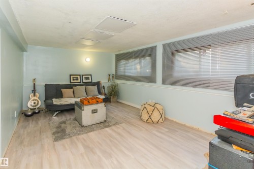 Spacious room featuring light wood-finish flooring, light blue walls with white trim, and multiple windows with horizontal blinds - 13208 128 Avenue Nw, Edmonton, AB - Indoor