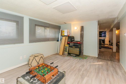 Lower level room featuring light wood-finish flooring, two rectangular windows with horizontal blinds, and a built-in wall sconce - 13208 128 Avenue Nw, Edmonton, AB - Indoor Photo Showing Other Room