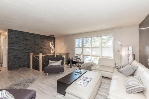 Spacious living area featuring a prominent dark stacked stone accent wall, light wood-finish flooring, and a large multi-pane window - 13208 128 Avenue Nw, Edmonton, AB - Indoor Photo Showing Living Room