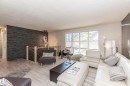 Spacious living area featuring a prominent dark stacked stone accent wall, light wood-finish flooring, and a large multi-pane window - 13208 128 Avenue Nw, Edmonton, AB  - Indoor Photo Showing Living Room 