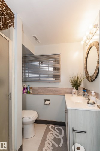 Bathroom featuring a wood-finish vanity with a white countertop, an oval mirror with a decorative frame, and a glass-enclosed shower - 13208 128 Avenue Nw, Edmonton, AB - Indoor Photo Showing Bathroom