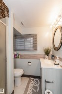 Bathroom featuring a wood-finish vanity with a white countertop, an oval mirror with a decorative frame, and a glass-enclosed shower - 