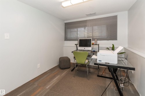 Room featuring a window with horizontal blinds, overhead fluorescent lighting, and a combination of carpet and wood-finish flooring - 13208 128 Avenue Nw, Edmonton, AB - Indoor Photo Showing Office