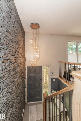 Entryway featuring a stacked stone accent wall, multi-tiered chandelier, and dark paneled door with frosted glass sidelight - 13208 128 Avenue Nw, Edmonton, AB - Indoor Photo Showing Other Room
