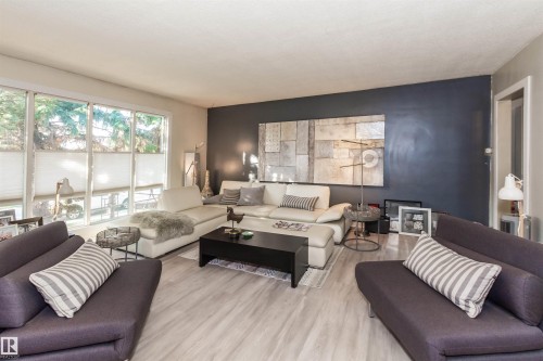 Spacious living area featuring large windows with cellular shades, light wood-finish flooring, and a contrasting accent wall - 13208 128 Avenue Nw, Edmonton, AB - Indoor Photo Showing Living Room