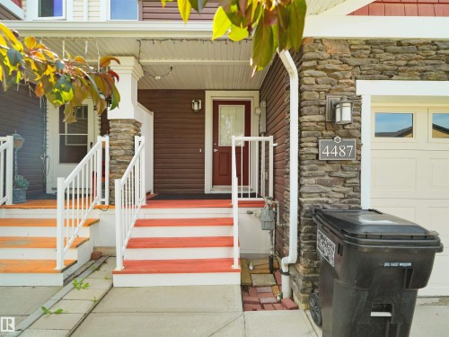 Exterior entrance featuring a rich brown siding, stone accents, white railings, and a red front door - 4487 Annett Common Sw, Edmonton, AB - 
