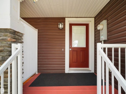 Entryway featuring a red paneled door with a glass insert, white door trim, brown siding, a complementary white railing, and a stone column base - 4487 Annett Common Sw, Edmonton, AB - Outdoor With Exterior