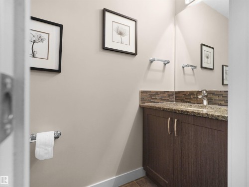 Vanity featuring a stone countertop, an undermount sink, and a multi-tone tile backsplash - 4487 Annett Common Sw, Edmonton, AB - Indoor Photo Showing Bathroom