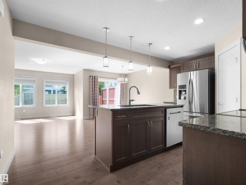 Kitchen featuring an island with a sink, pendant lighting, stainless steel appliances, dark wood-finish cabinetry, and granite countertops - 4487 Annett Common Sw, Edmonton, AB - Indoor Photo Showing Kitchen With Upgraded Kitchen