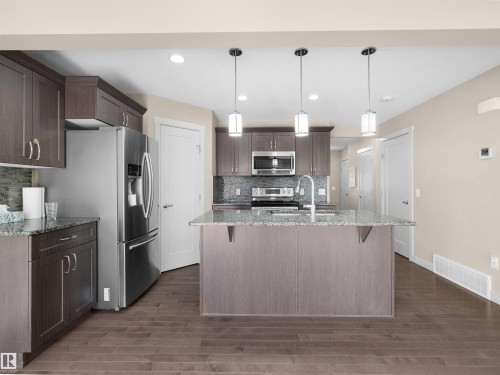 Kitchen featuring wood-finish flooring, dark wood cabinetry, and light-toned countertops - 4487 Annett Common Sw, Edmonton, AB - Indoor Photo Showing Kitchen With Stainless Steel Kitchen With Upgraded Kitchen
